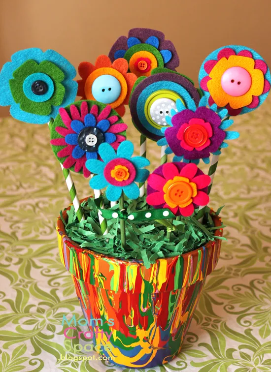 A picture of a flower pot that has been painted with various colors of paint in a marbled design. There is crinkle grass and felt flowers in the pot.